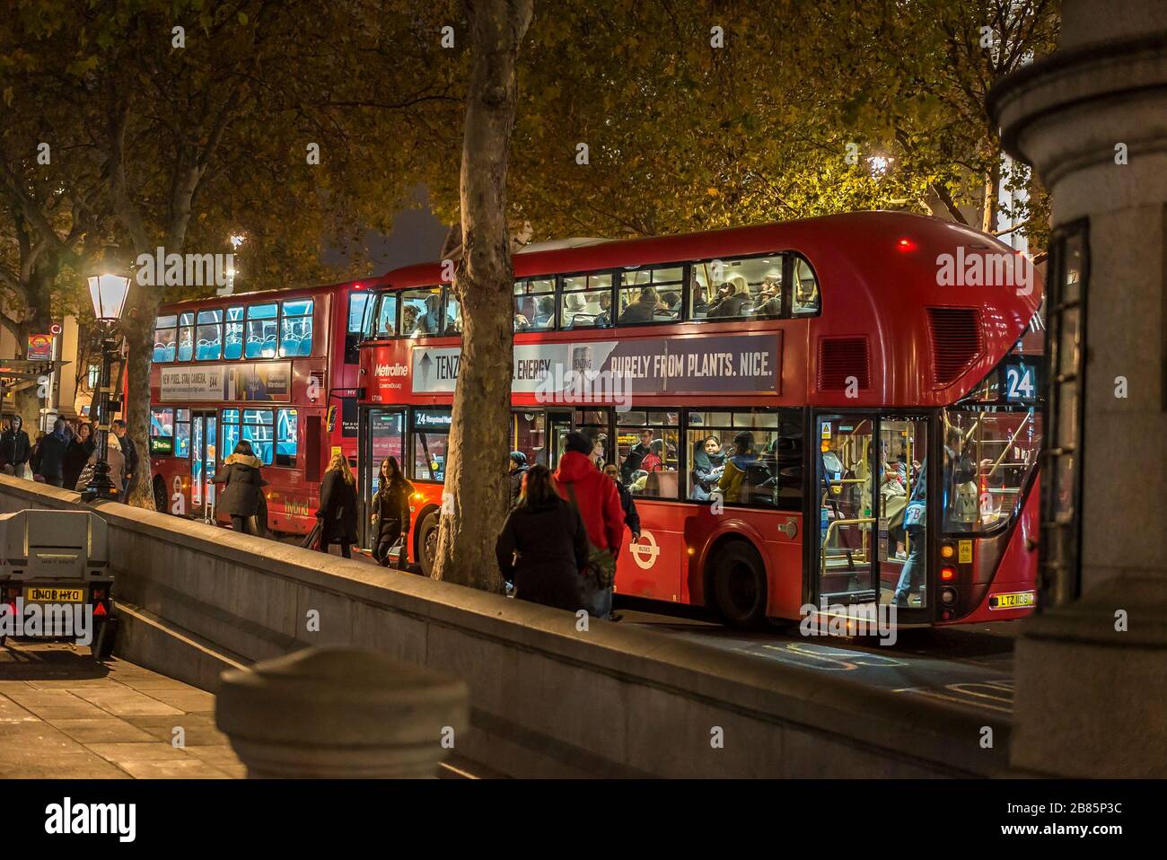 Seitenansicht, rote Doppeldecker-London-Busse geparkt, Trafalgar Square, Central London UK nachts. Buspassagiere, die in den öffentlichen Busverkehr einsteigen und diese abfahren. Stockfoto