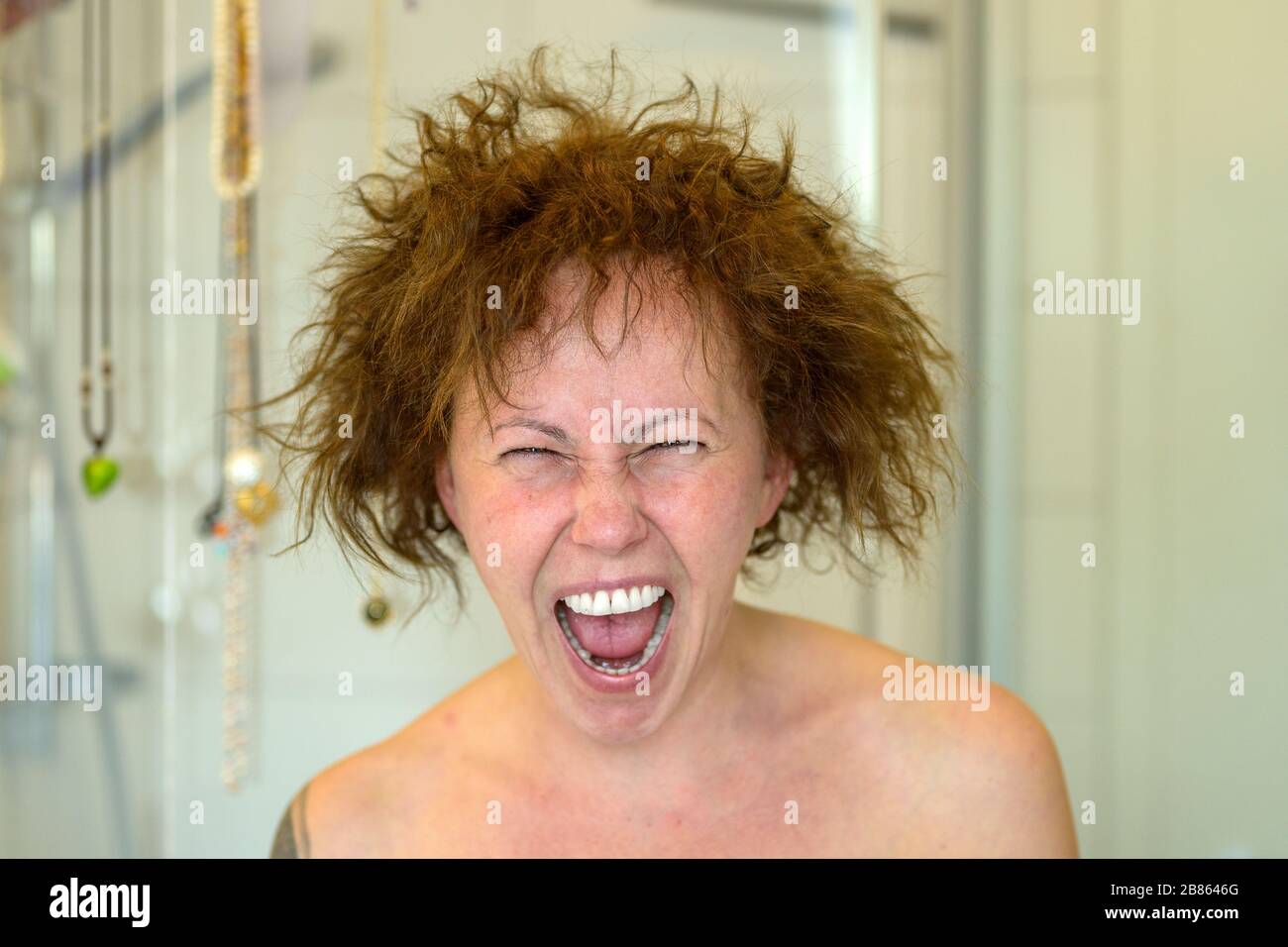 Frau, die an einem schlechten Haartag frustriert schreit und nach dem Duschen in einem Nahporträt ihre unbeweglichen lockigen Haare in alle Richtungen fliegen Stockfoto
