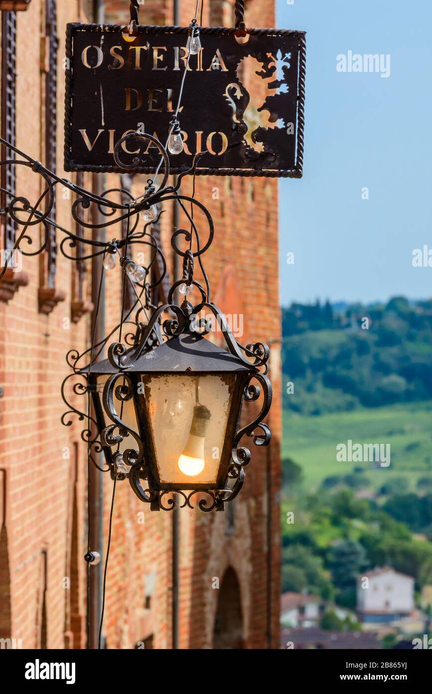 Certaldo, Toskana / Italien: Eine verzierte Straßenbeleuchtung und ein Metallzeichen der Osteria del Vicario im mittelalterlichen Oberteil der Stadt, genannt Certaldo Alto. Stockfoto