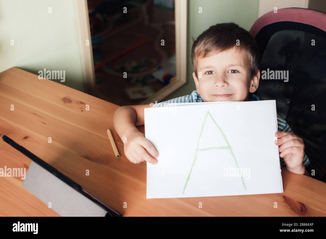 Glücklicher zufriedener Junge zeigt Seite mit dem schriftlichen Brief A, Hausunterricht Stockfoto