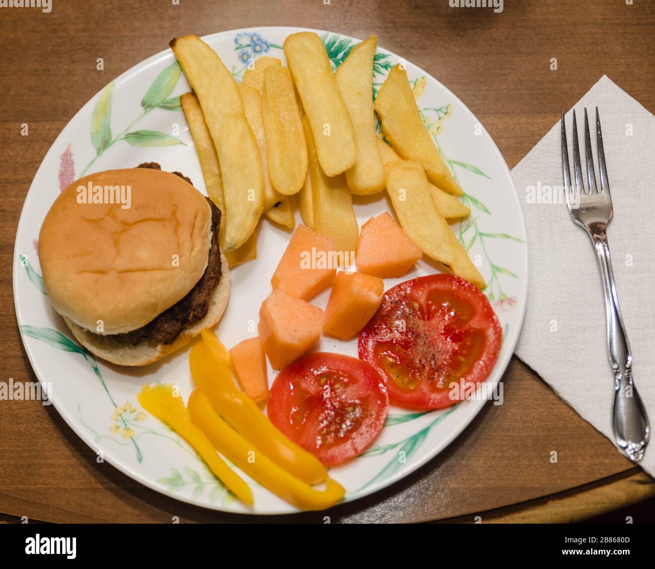 Das erste Frühlingsabendessen, Burger, Pommes, Melone, Tomaten und Paprika Stockfoto