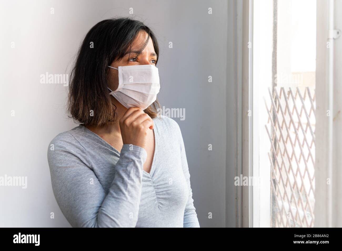 Porträt der jungen Frau mit Gesichtsmaske in Quarantäne aufgrund des Corona-Virus in ihrem Haus mit trauriger und besorgter Ausdrucksweise aufgrund der Isolation Stockfoto