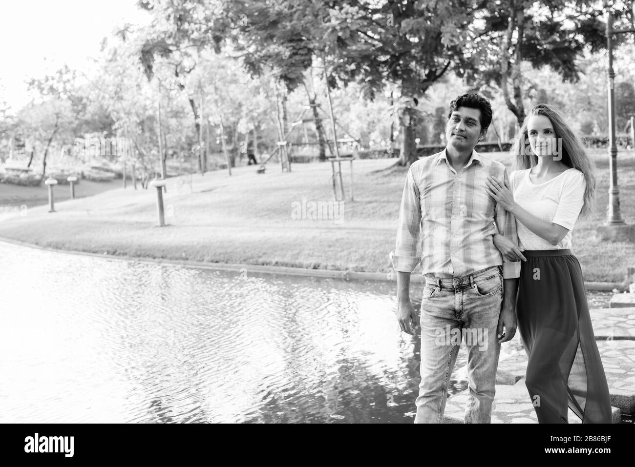 Multiethnisches Paar denkt, während es auf einem Steinpfad mitten im See im Park steht Stockfoto