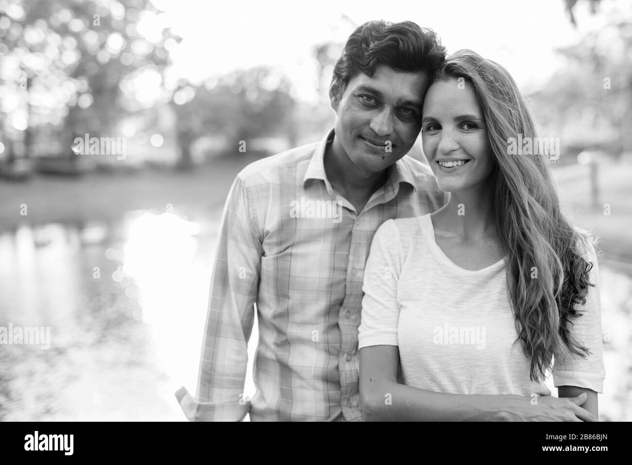 Fröhliches multiethnisches Paar lächelt und verliebt gegen den malerischen Blick auf den See im Park Stockfoto