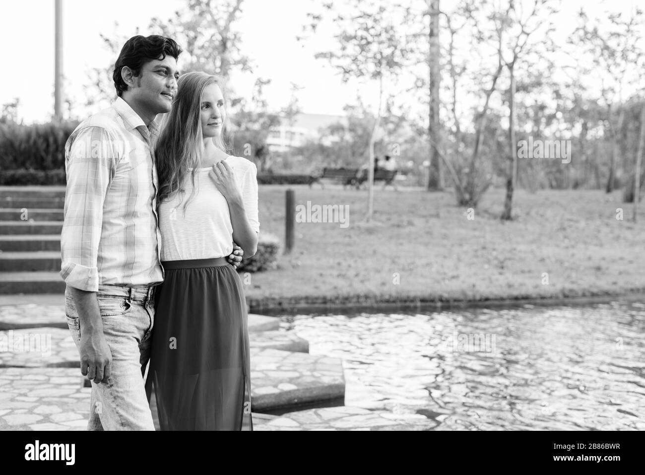 Multiethnisches Paar steht und denkt auf dem Steinweg mitten im See gegen den Blick auf den Park Stockfoto