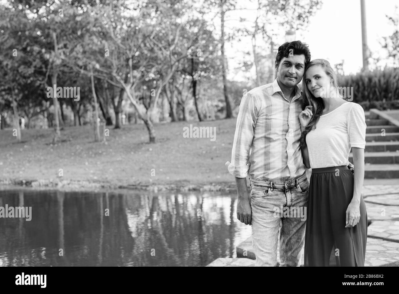 Ein Vielvölkerpaar steht auf einem Steinpfad mitten im See gegen den Blick auf den Park Stockfoto