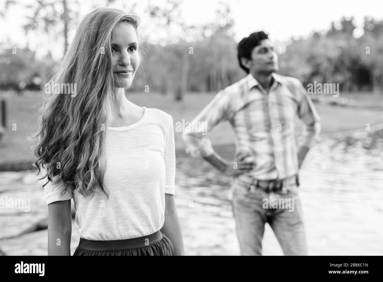 Schöne Frau, die mit einem indianischen Mann denkt, der auf einem Steinpfad mitten im See im Park zusammensteht Stockfoto