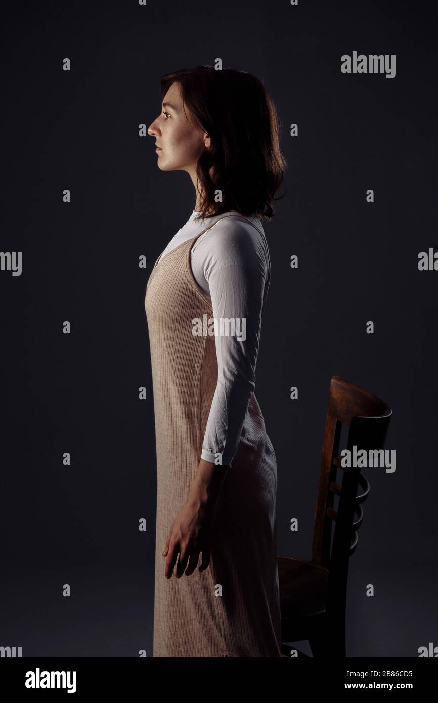 Ein Mädchen in einer Zwangsjacke steht und freut sich. In der Nähe befindet sich ein Holzstuhl. Stockfoto