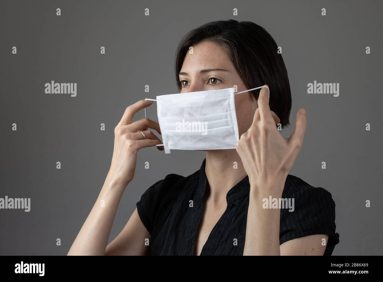 Brünette Frau mit hygienischer Maske zur Vorbeugung von Infektionen, Atemwegserkrankungen wie Grippe, 2019-nCoV auf grauem Hintergrund. Konzept für das Gesundheitswesen. Stockfoto