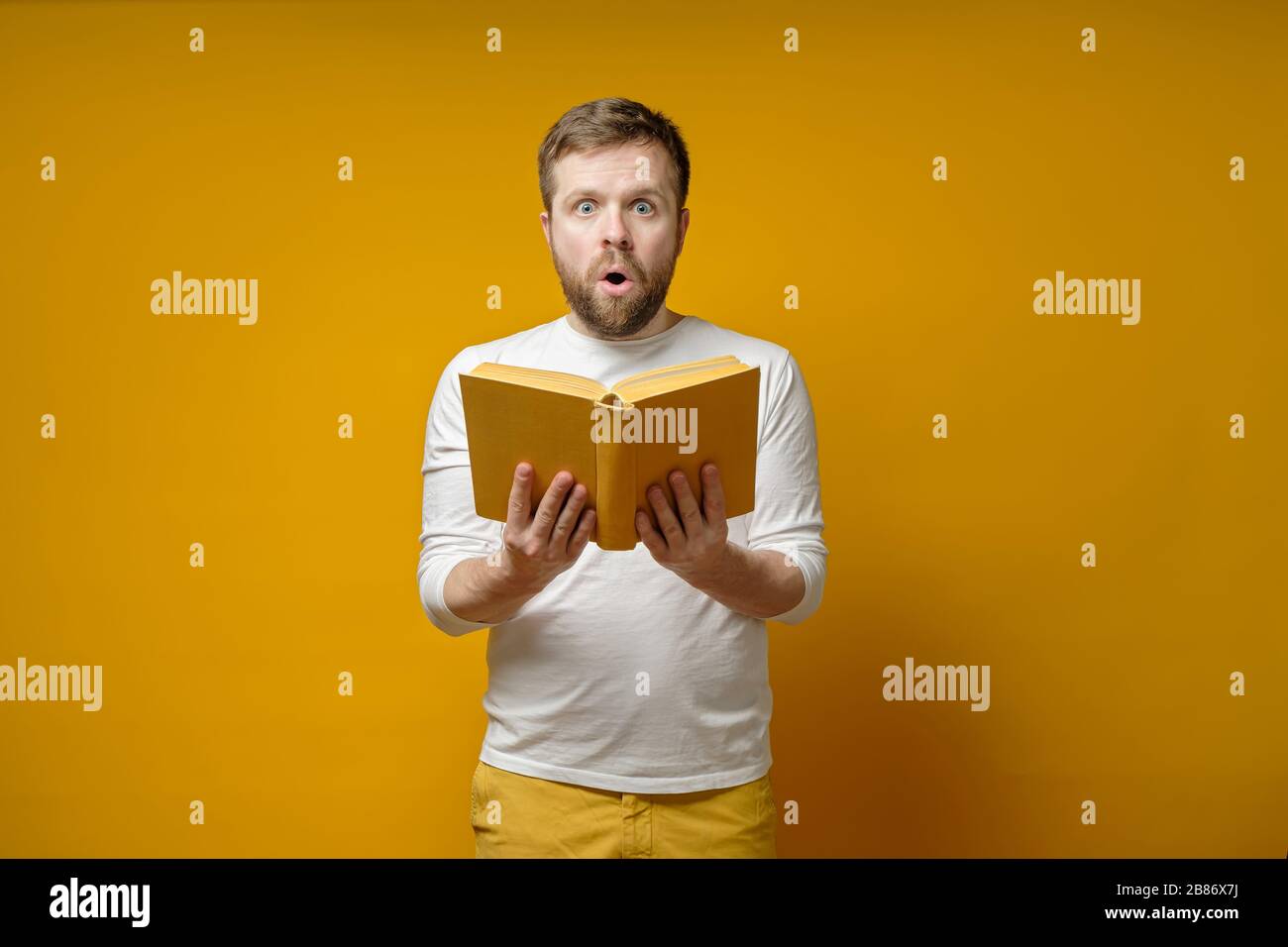 Der attraktive Mann mit einem Buch in der Hand ist fasziniert von dem, was er gelesen hat und überrascht aussieht. Bildungskonzept. Stockfoto