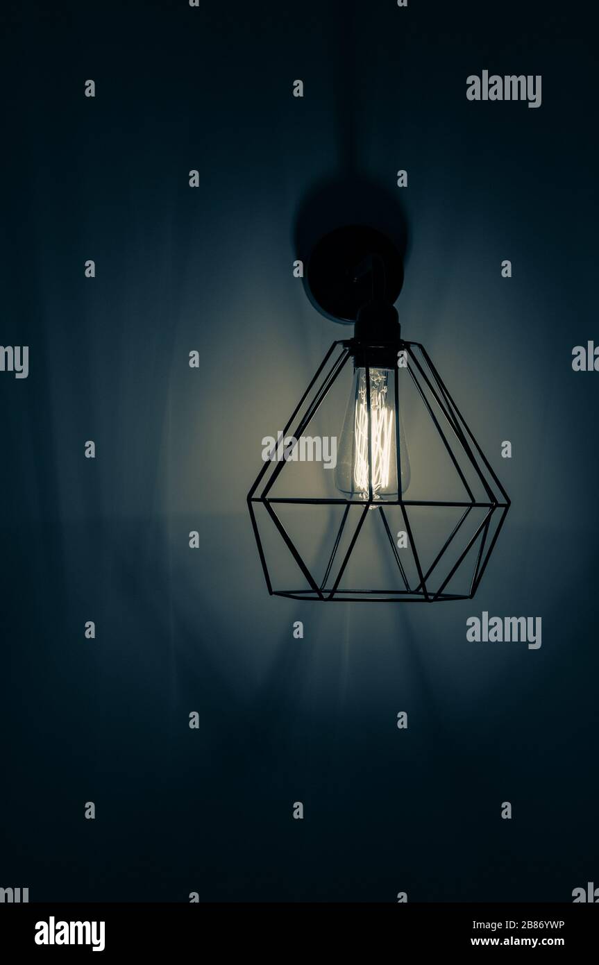 Dunkelblaues Filterfoto der Pendelleuchte mit Lampenschirm in Form von Diamantdraht Karkasse mit Glühbirne innen. Glühfaden in Lampe Stockfoto