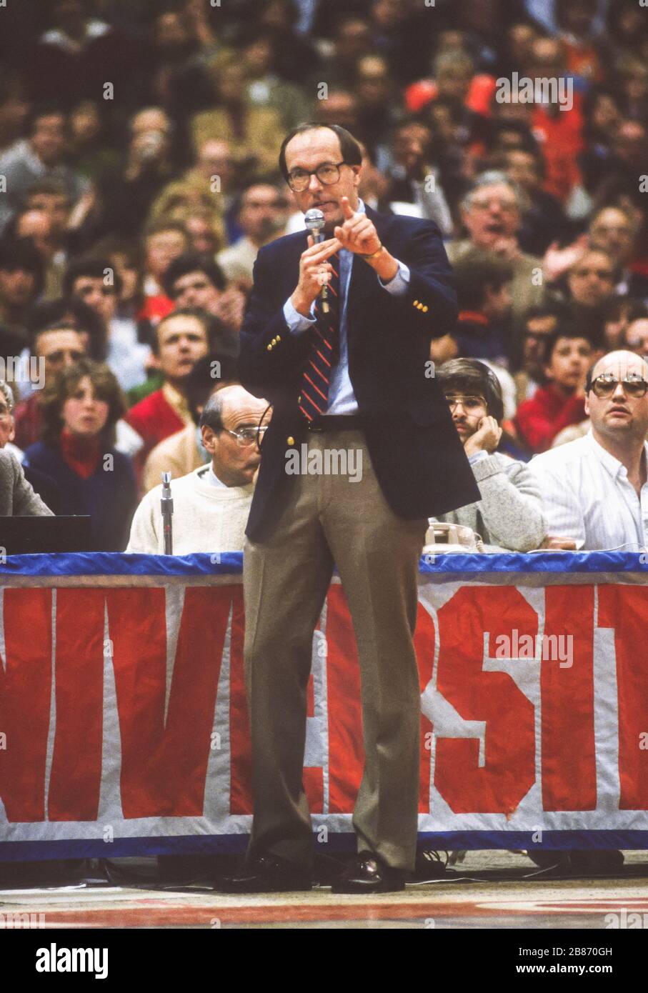 SYRACUSE, NEW YORK, USA, 1985 - der Basketballtrainer der Syracuse University Jim Boeheim nimmt ein Mikrofon, um die Menge zu warnen, während des Georgetown Spiels 1/28/85 keine Gegenstände auf den Platz zu werfen. Stockfoto