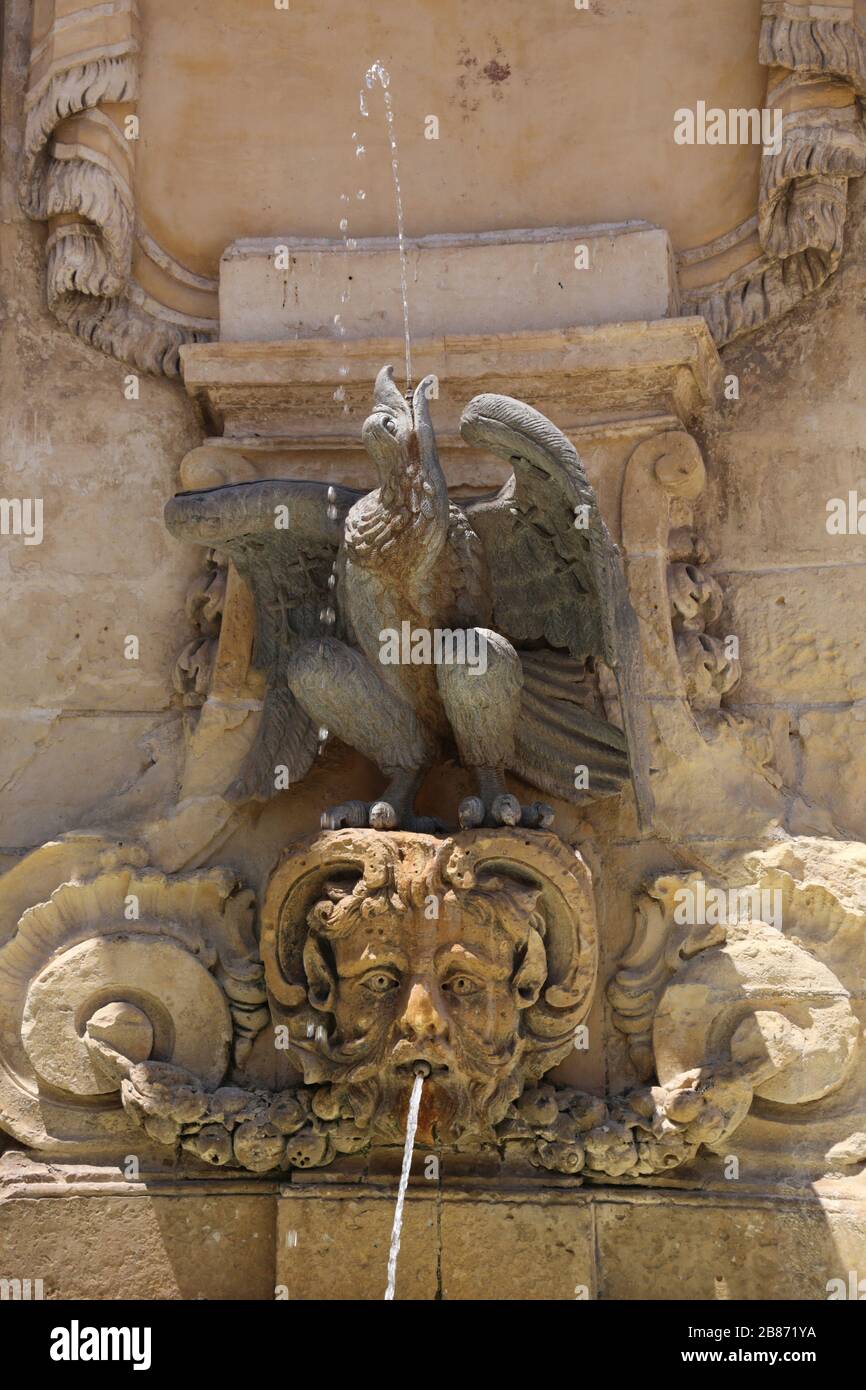 Valletta. Malta. Aus Sandstein gefertigter Brunnen am St.-Georgs-Platz mit Figur des Adlers und Faun's Kopf. Ecke des alten Hauptwachtgebäudes. Stockfoto