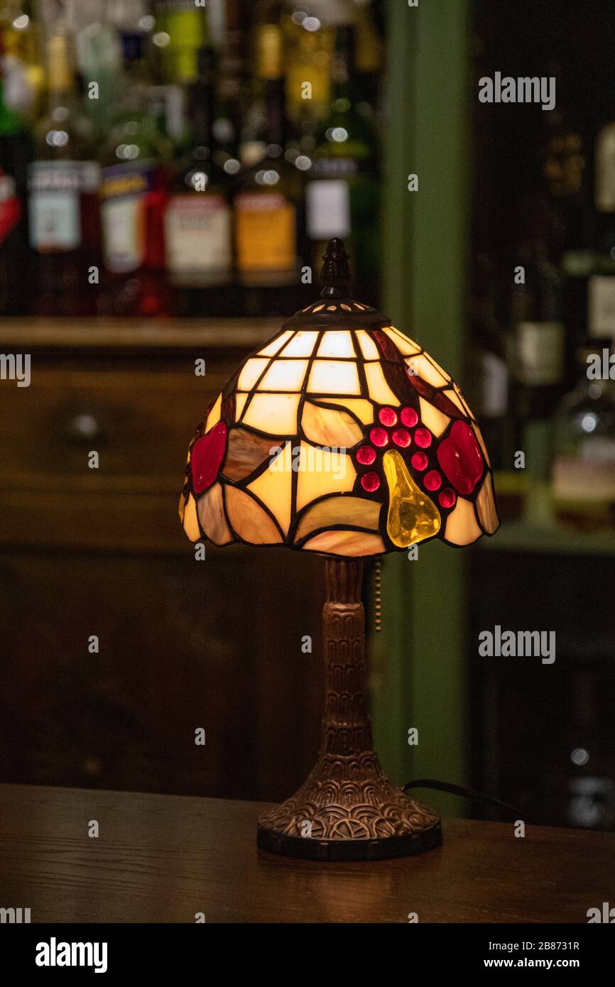 Retro-Tischleuchte mit Lampenschirm aus Buntglas im Nahbereich auf unscharfem Hintergrund der Leiste. Glühende Mosaiklampe in Form einer Kuppel. Vintage-Tischleuchte Stockfoto