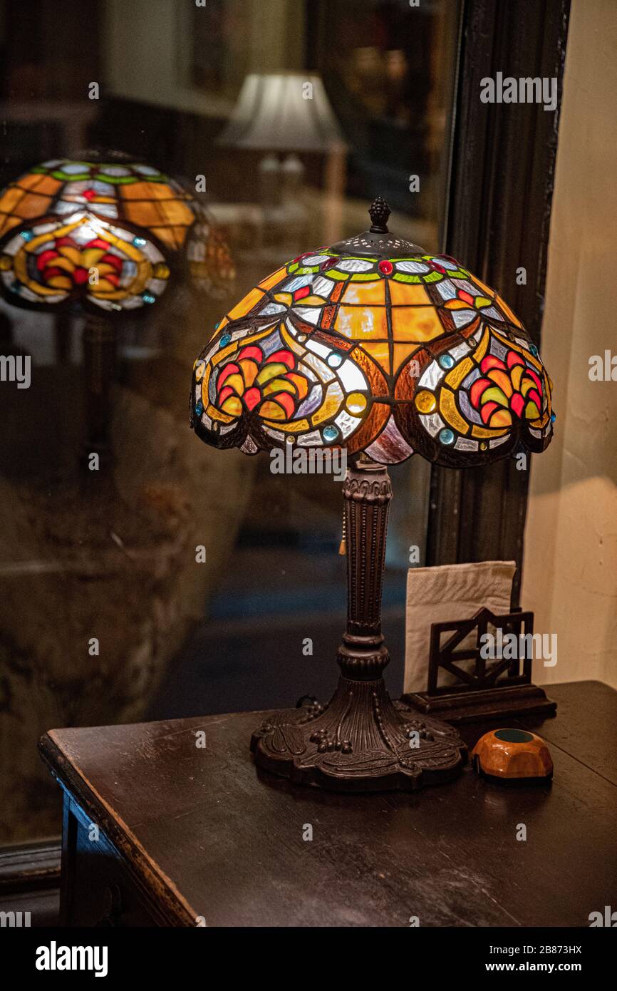 Antike Tischleuchte mit Lampenschirm aus Buntglas im Dunkeln verschwommener Hintergrund. Glühende Mosaiklampe in Form einer Kuppel. Vintage-Tischleuchte. Stockfoto