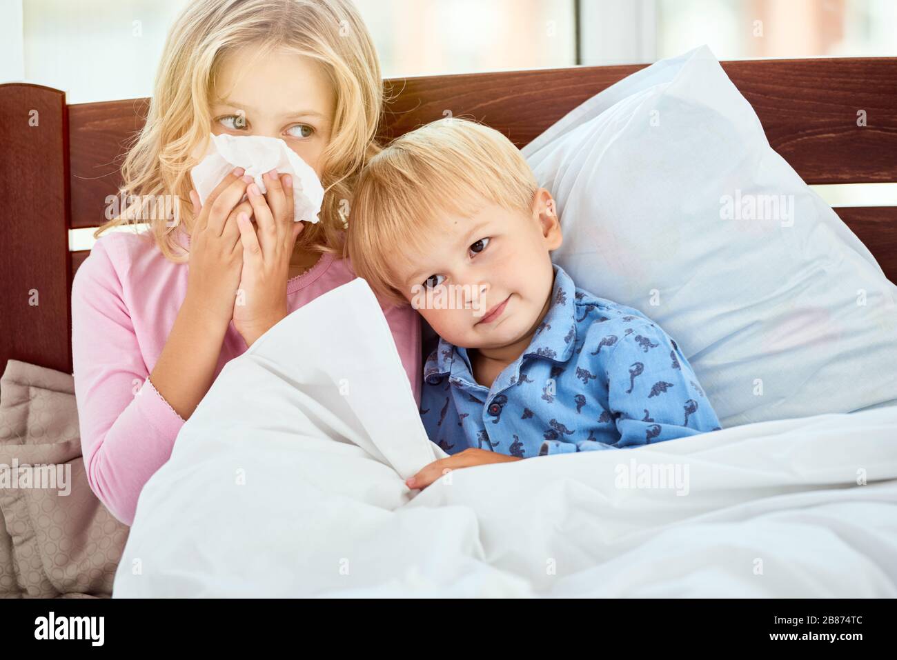 Kleine Schwester und Bruder mit nassen Nasen, die an Grippe oder Kälte leiden, während sie zu Hause im Bett liegen. Viruserkrankung. Coronavirus Konzept. Kranke Familie zu Hause. Gesundheitskonzept Stockfoto