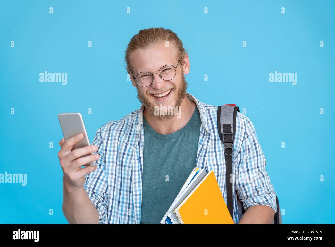 Fröhlicher Mann Student lacht halten Telefon isoliert auf blauem Hintergrund. Stockfoto