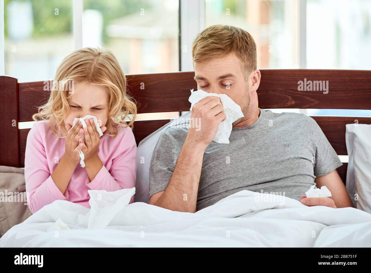 Vater und Tochter leiden an Grippe oder Kälte und wischen Nasen, während sie zu Hause im Bett liegen. Viruserkrankung. Coronavirus Konzept. Kranke Familie zu Hause. Gesundheitskonzept Stockfoto