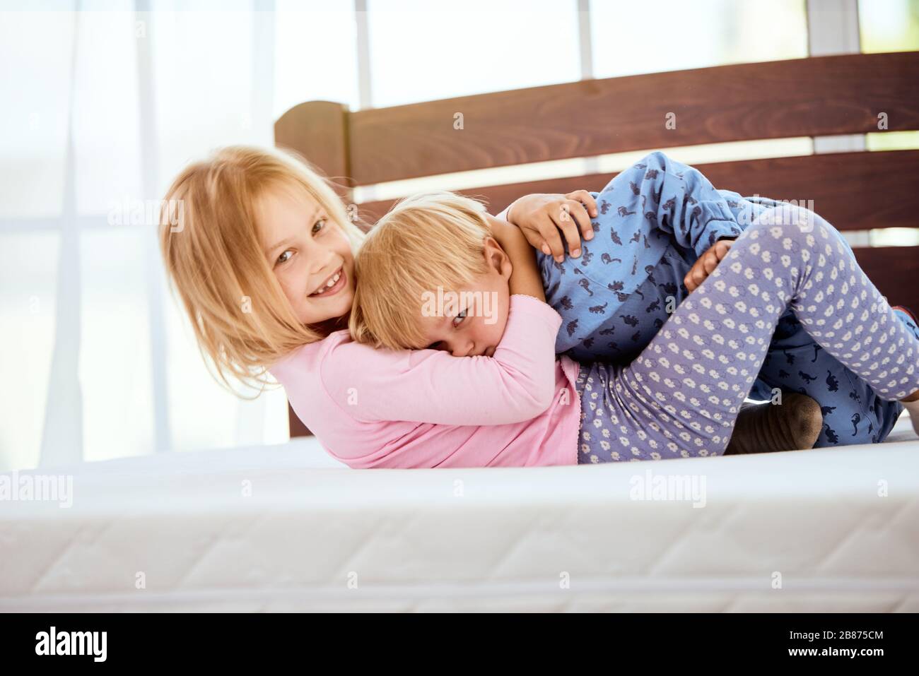 Glückliche kleine Schwester und Bruder im Schlafanzug spielen und Spaß beim liegen auf einer großen bequemen weißen Matratze im Schlafzimmer haben. Glückliche Familie zu Hause Stockfoto