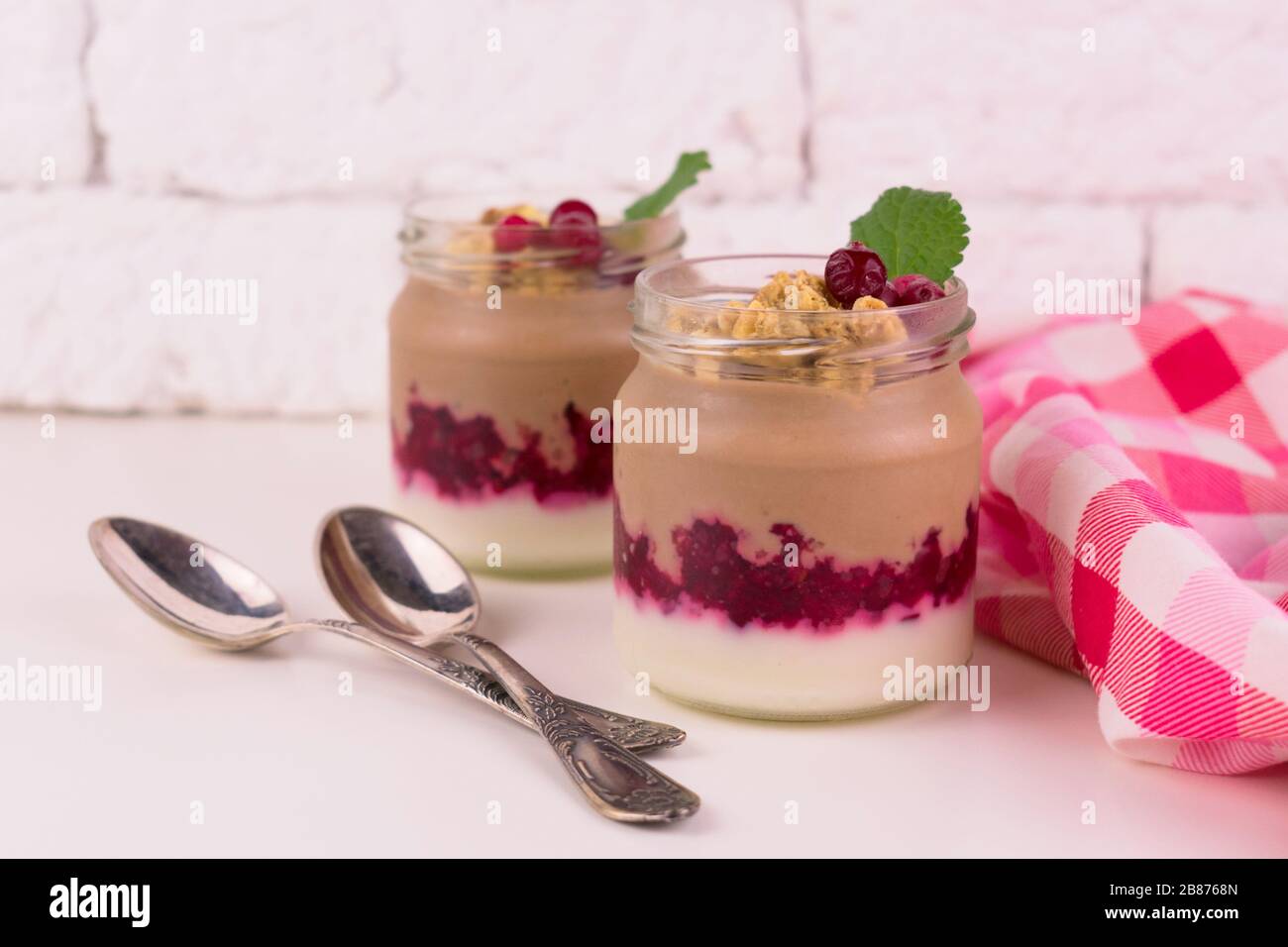 Zwei Portionen Schoko-Vanille-Pudding mit Beeren und einem Glas auf weißem Hintergrund. Stockfoto
