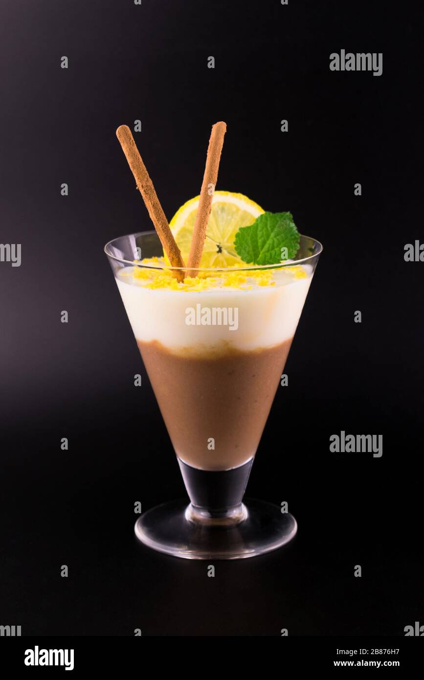 Schokolade und Zitronendessert (Pudding) sind mit Zitronenschale auf schwarzem Grund dekoriert. Stockfoto