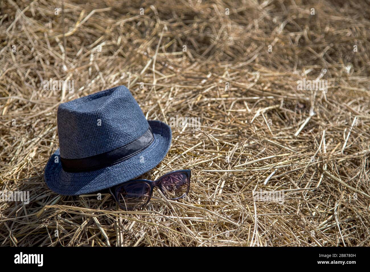 Blauer Hut und Sonnenbrille auf trockenem Strohhalm am Standort des Landes Stockfoto