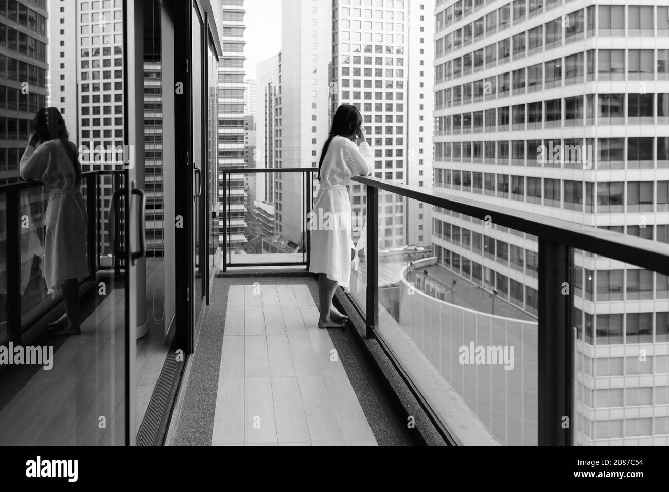 Junge, schöne asiatische Frau, die vom Balkon aus den Blick auf die Stadt genießt Stockfoto