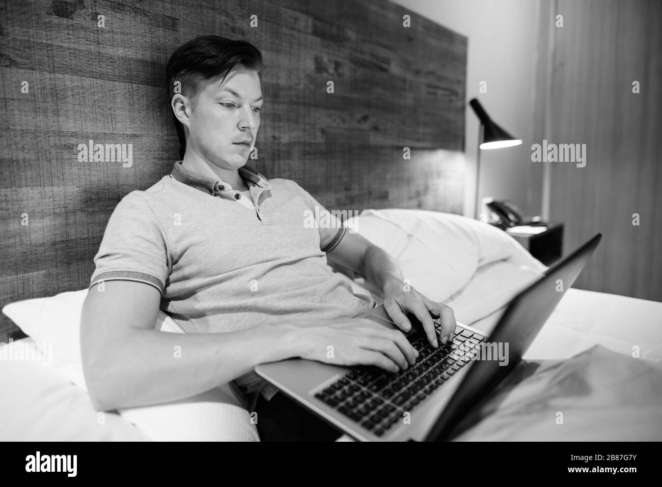 Junger, gutaussehender Mann, der einen Laptop verwendet, während er sich im Schlafzimmer wohlfühlt Stockfoto