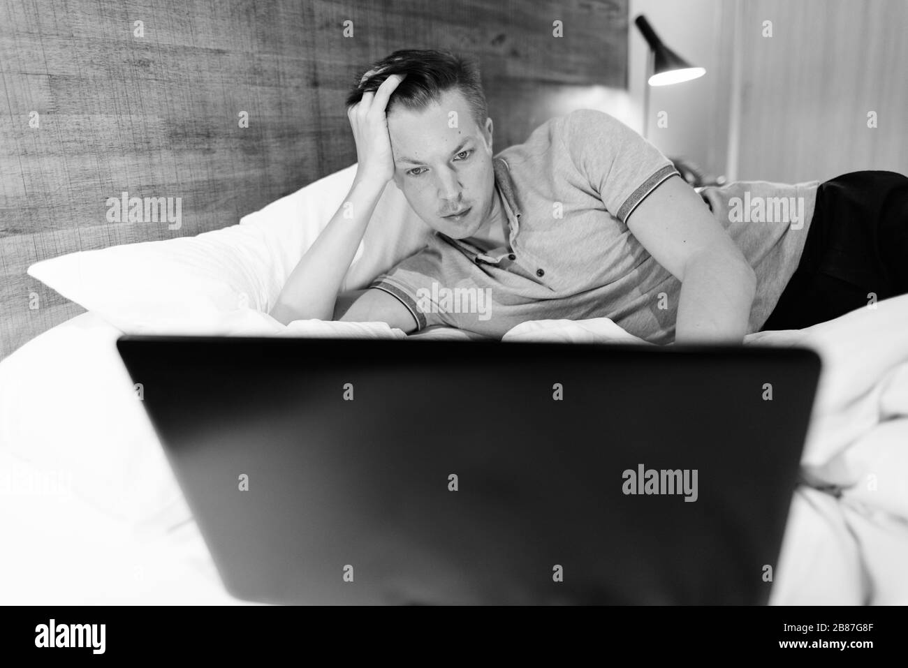 Junger, gutaussehender Mann, der einen Laptop verwendet, während er sich im Schlafzimmer wohlfühlt Stockfoto