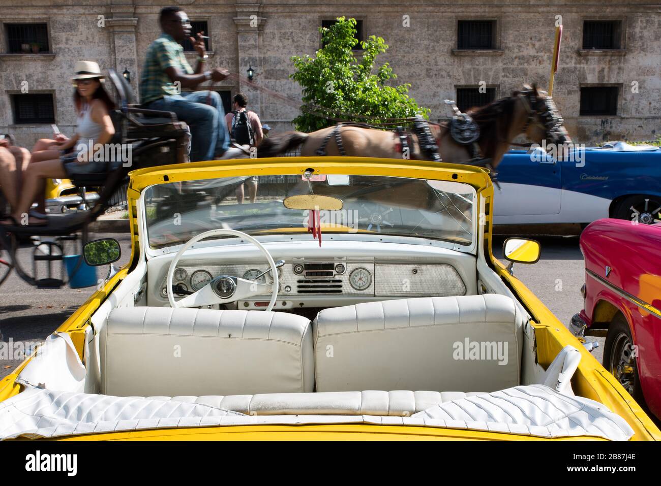 Gelber, vertauschbarer amerikanischer Oldtimer geparkt und Pferdetrainer vorbeifahrend. Havanna Street-Szene, Kuba. Stockfoto