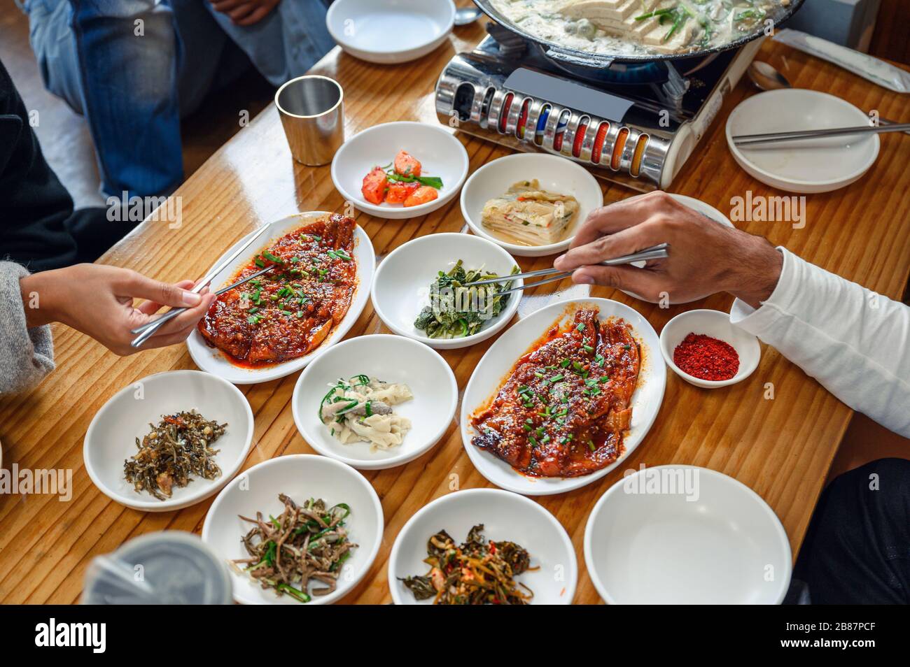 Hände, die Essstäbchen an koreanischen Lebensmitteln auf Holztisch halten Stockfoto