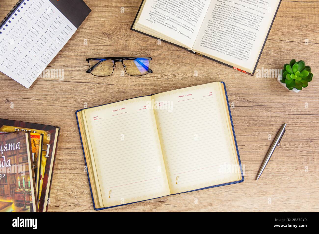 Arbeitsfläche zurück zur Schule und zum Bildungskonzept auf einem alten Holztisch mit Vintage leerem Notizblock und Stapel von Buch, Glas, Bleistift, grüner Pflanze Stockfoto