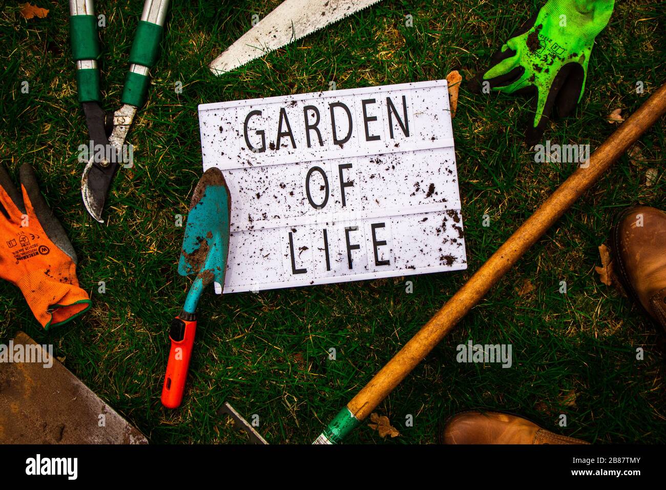 Draufsicht auf einen Leuchtkasten, der von Werkzeugen eines Gärtners und des Gewänders selbst umgeben ist. Der Leuchtkasten hat "Garten des Lebens" ausgeschrieben. Lifestyle. Stockfoto