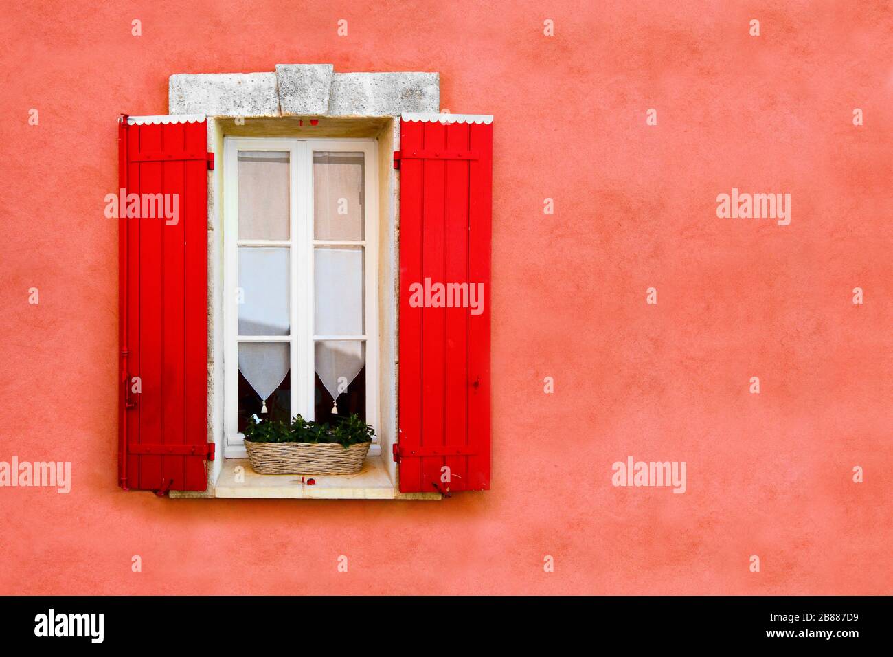 Rotes Fenster mit Blenden gegen die rot ockerfarbene Wand Stockfoto