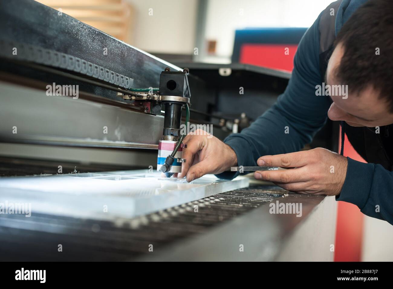 Elektroingenieur repariert einen Laserschneidkopf an einer großen CNC-Computernumeriermaschine für Druck- und Schneidmaschinen Stockfoto