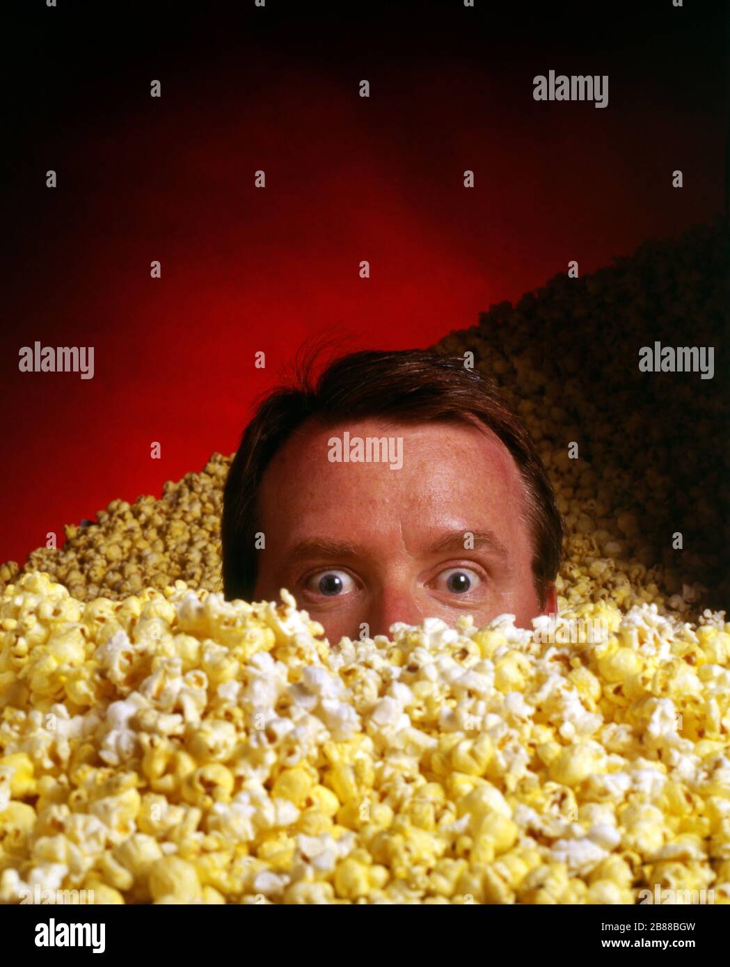 Kopf knallt aus einem Meer von Popcorn, weiten Augen Stockfoto