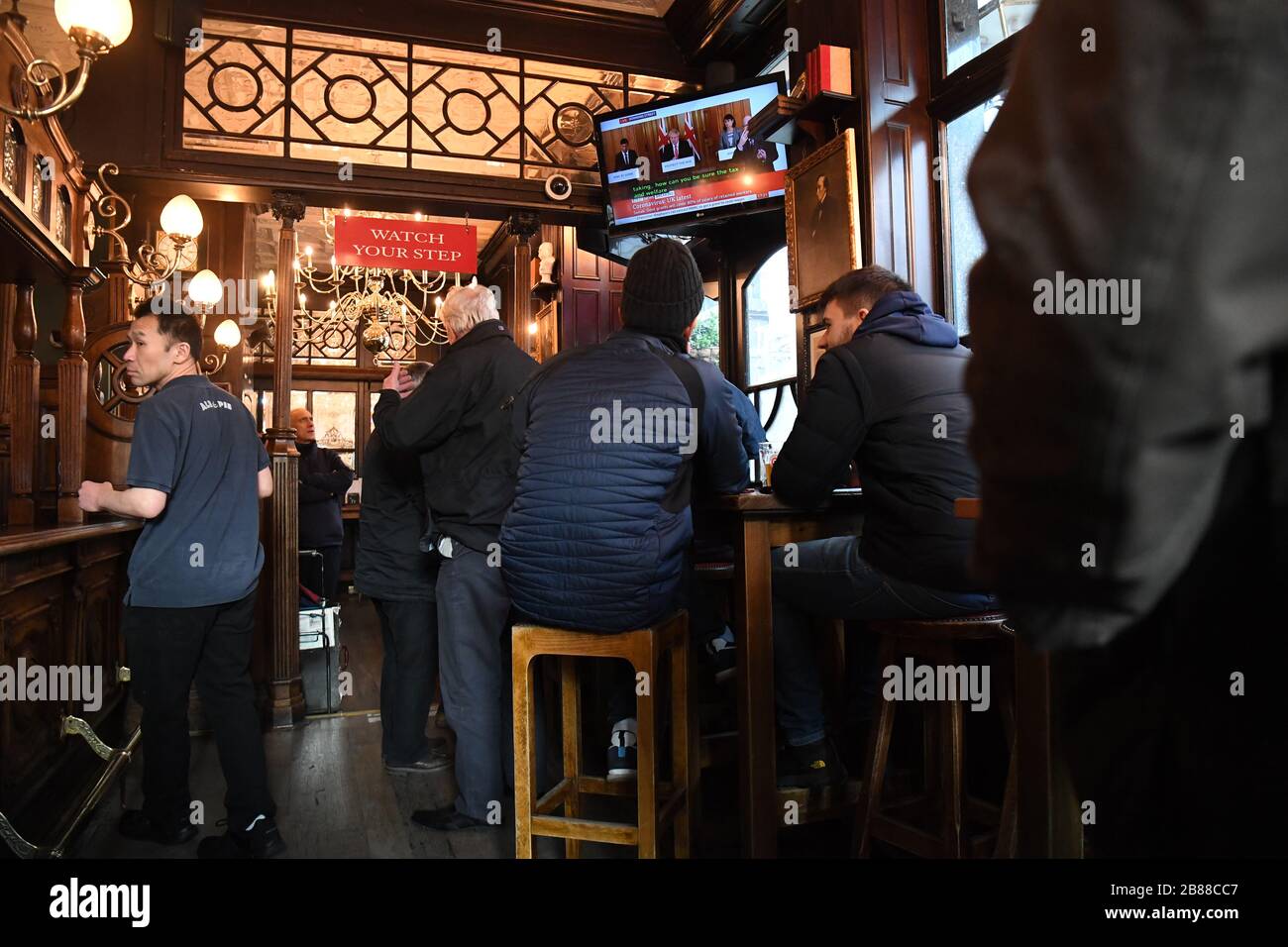 Kunden im Red Lion Pub in Westminster in London sehen sich das Fernsehen an, während Boris Johnson Pubs und Restaurants im ganzen Land bestellt, um heute Abend zu schließen, da die Regierung beispiellose Maßnahmen zur Deckung des Lohns von Arbeitern ankündigte, die ansonsten aufgrund des Ausbruchs des Coronavirus ihren Arbeitsplatz verlieren würden. Stockfoto