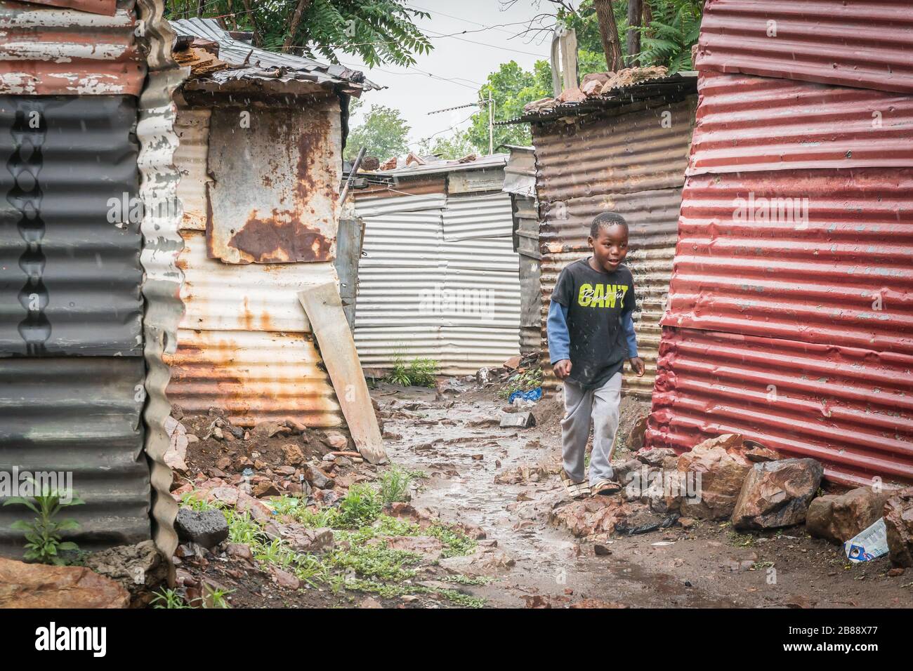 Johannesburg, Südafrika - 4. Dezember 2019 - ein Junge läuft im Regen die Straße in Soweto Slums hinunter Stockfoto