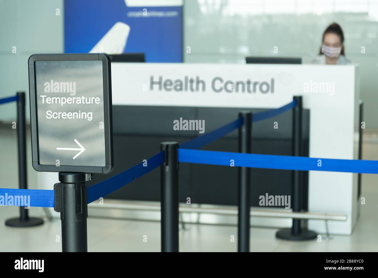 Temperatur-Screening-Schild am Flughafen mit einer Frau, die eine Maske trägt, die am Schalter der Gesundheitskontrolle sitzt Stockfoto