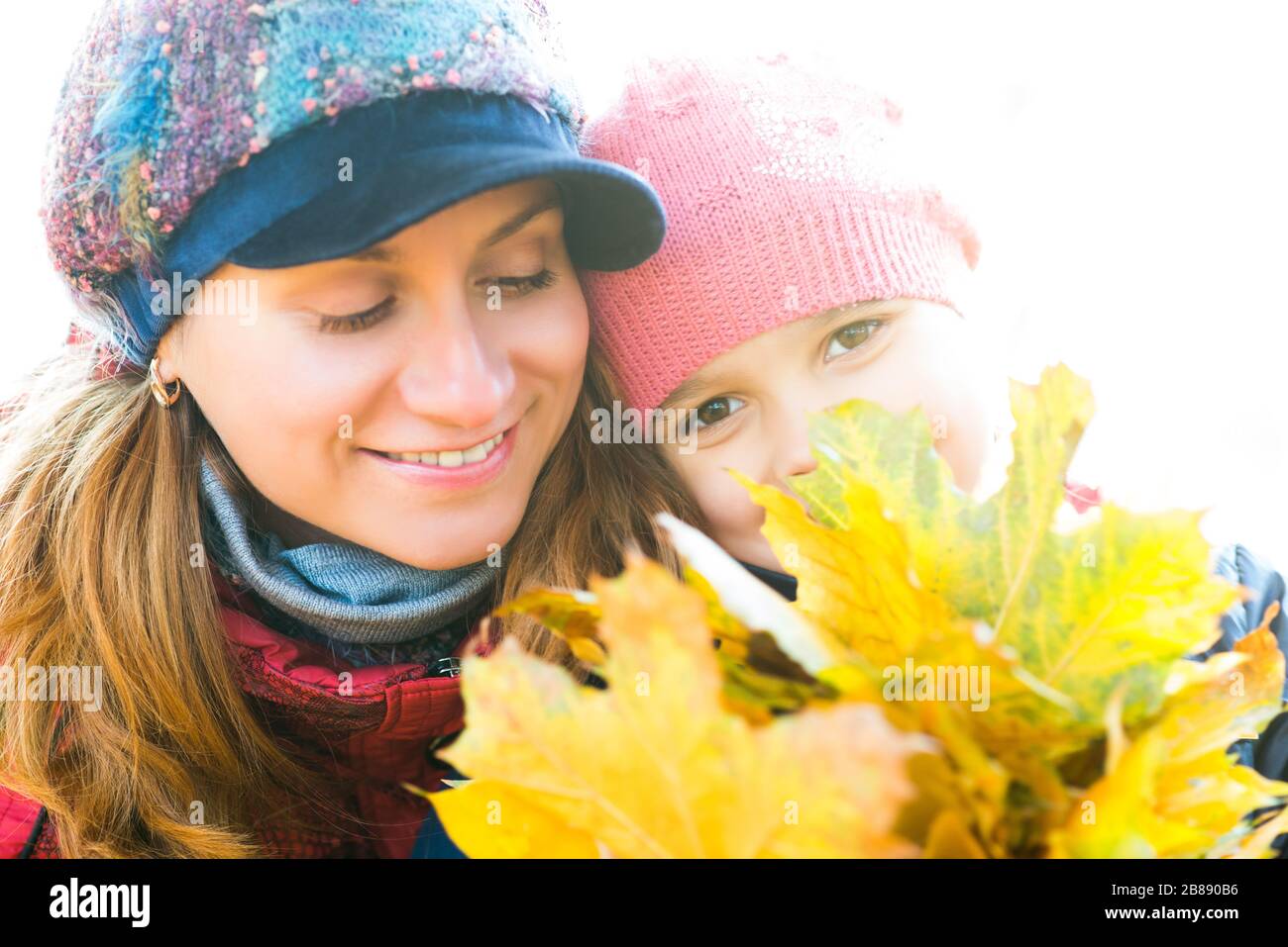 Porträt einer fröhlichen, schönen jungen Mutter mit ihrer hübschen Tochter, die gelbe Blätter aus Ahorn im Herbst in den Händen hält, während sie im Park spazieren ging. Konz Stockfoto