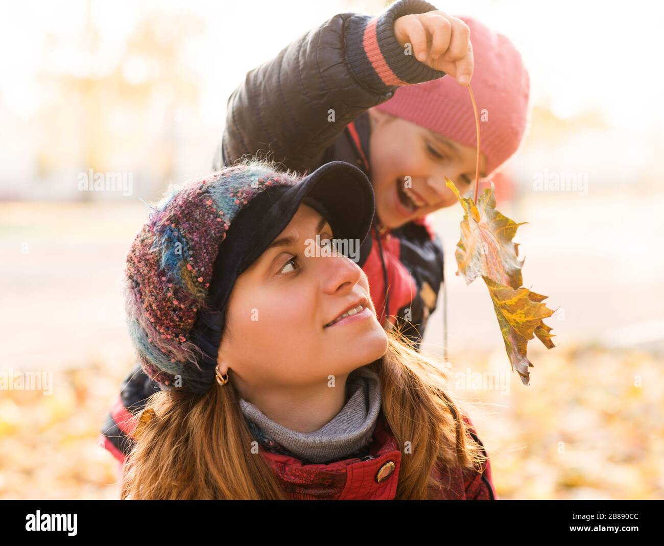 Porträt einer fröhlichen, schönen jungen Mutter mit ihrer hübschen Tochter, die gelbe Blätter aus Ahorn im Herbst in den Händen hält, während sie im Park spazieren ging. Konz Stockfoto