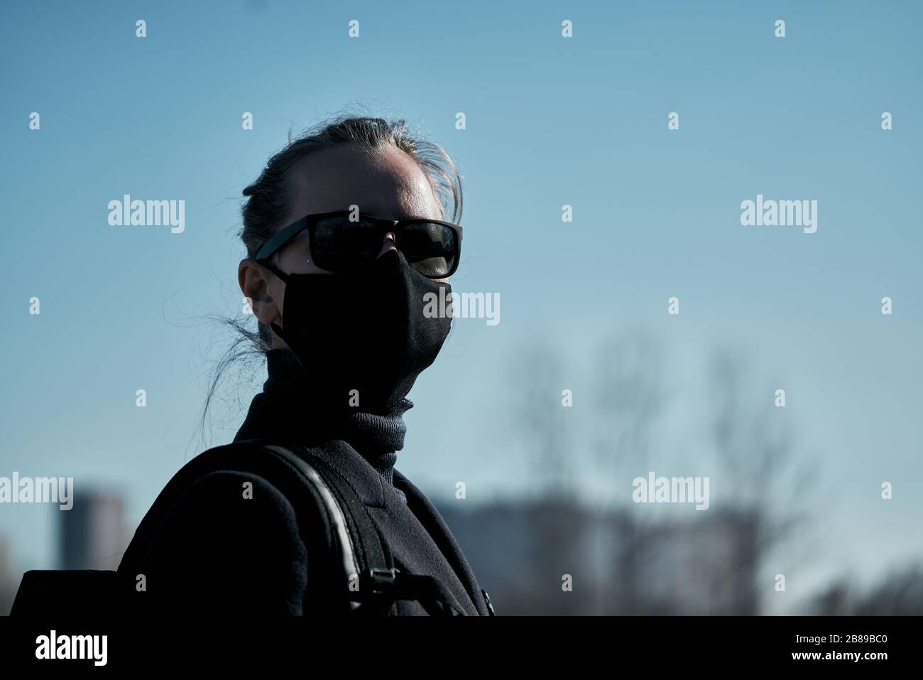 Junges Mädchen in schwarzer Schutzmaske und schwarzer Sonnenbrille auf der Straße, schützt vor dem Virushintergrund, schwarzer, schwarzer Maske, Atemschutz Stockfoto