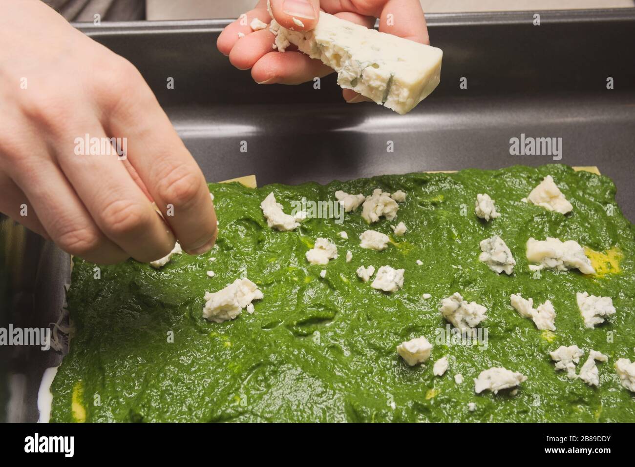 Hausfrau händigt dem rohen Spinat Lasagna den schimmeligen Käse aus Stockfoto