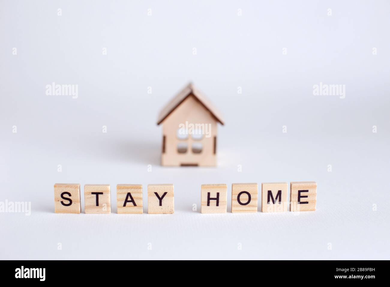 Modell eines Holzhauses und Holzbriefe mit der Aufschrift Stay Home...Stay at home, um das Infektionsrisiko zu verringern und das Virus zu verbreiten. Safe, ST Stockfoto