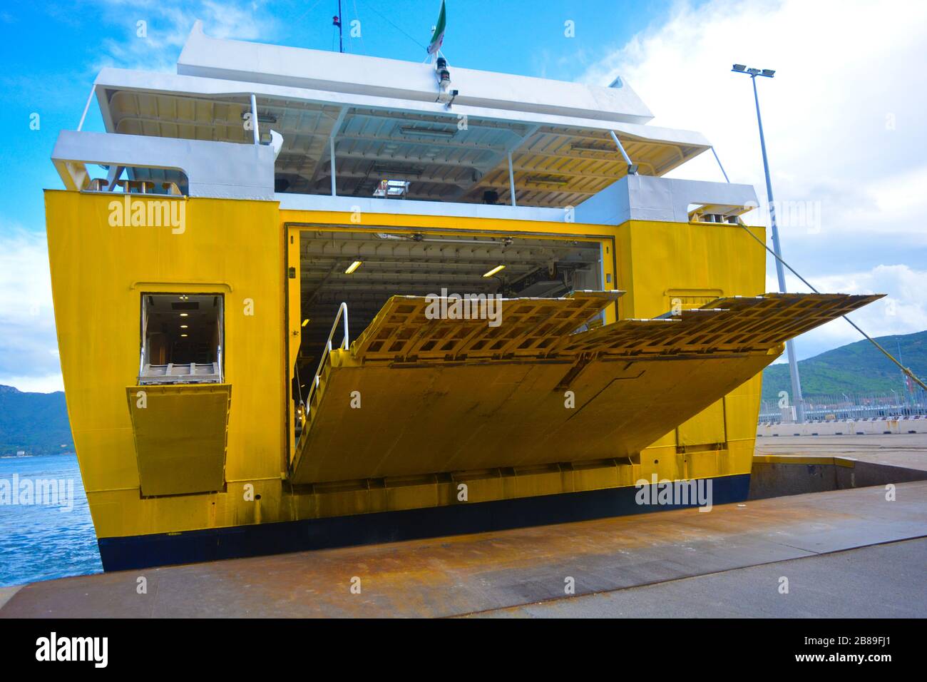 Das Heck einer großen gelben Fähre, die zum Hafen anfährt und sich auf die Ausschiffung vorbereitet. Die Auffahrt geht am Kai des Hafens hinunter. Ruhiger Tag Stockfoto