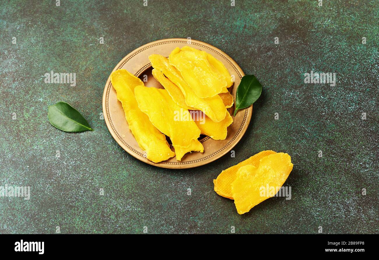 Getrocknete Mango-Früchte mit frischen Blättern auf grünem Grund. Mango in gelber Scheiben. Stockfoto