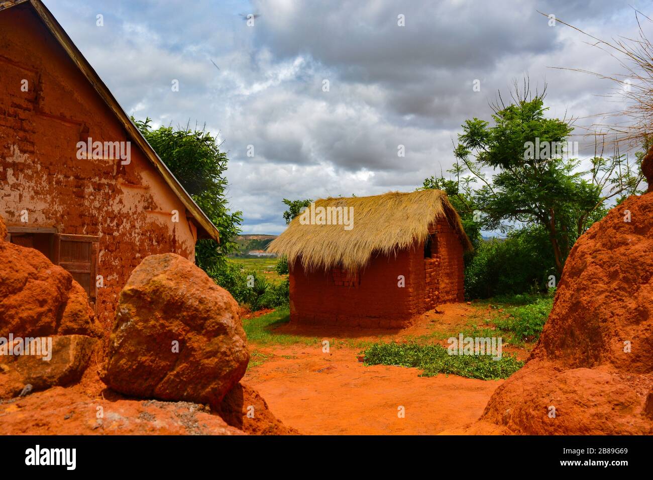 Ein afrikanisches orangenes Schlammhaus. In einem kleinen, abgelegenen, madagassischen Dorf ein einfaches Haus mit Wänden aus Schlamm, Dach aus Strohhalmen, Feldweg. Gemütliches Zuhause Stockfoto