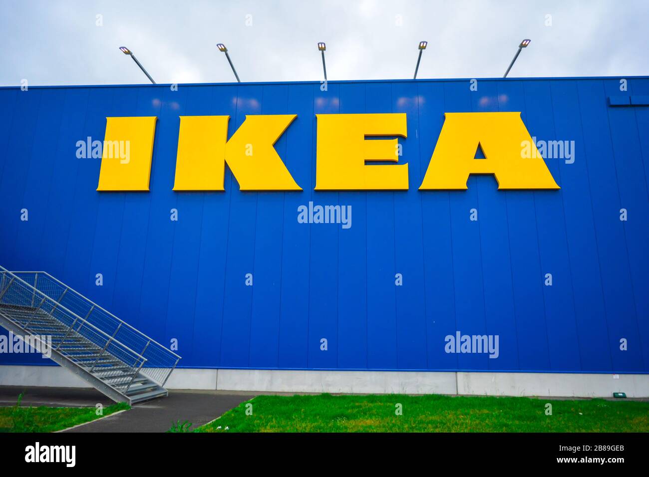 Nahaufnahme eines Ikea-Zeichens. Fassade der berühmten schwedischen Möbelhauskette. Davor ein schönes grünes Rasenfeld und eine Metallleiter. Stockfoto