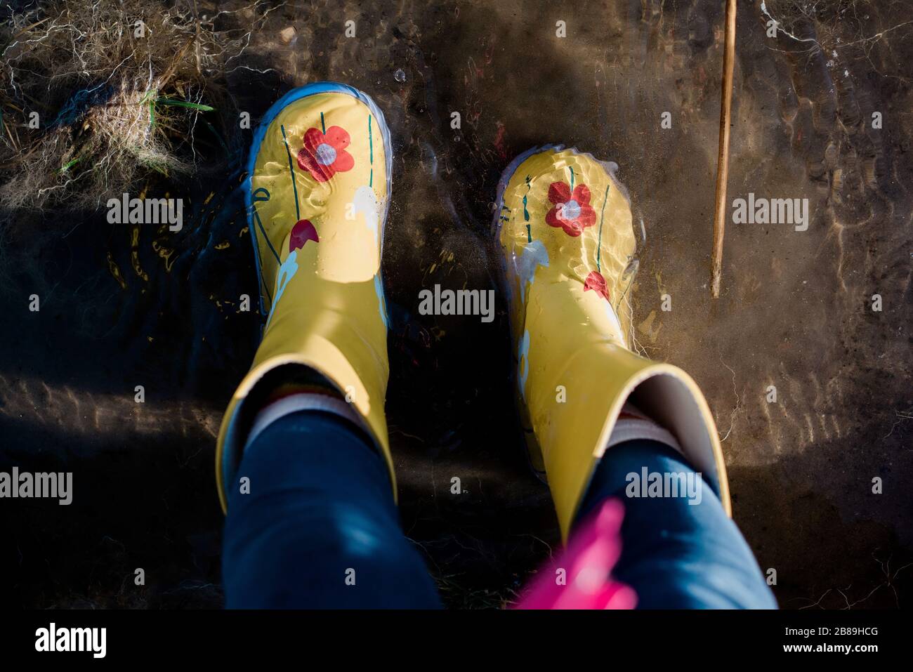 Childs Füße in Regenstiefeln in einer Pfütze aus Wasser und Schlamm Stockfoto