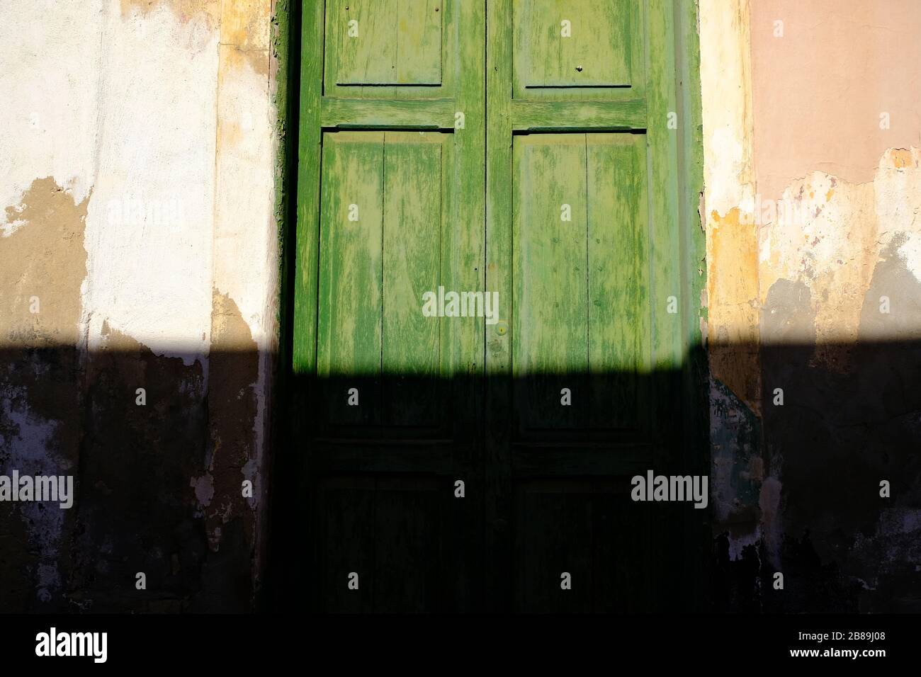 Grüne Grungentür eines alten Hauses, direkte warme Sonneneinstrahlung mit hartem Schatten, die untere Rahmenhälfte versteckt, Architekturdetails, Latino-Viertel. Stockfoto Grüne Grungentür eines alten Hauses, direkte warme Sonneneinstrahlung mit hartem Schatten, die untere Rahmenhälfte versteckt, Architekturdetails, Latino-Viertel. Stockfoto